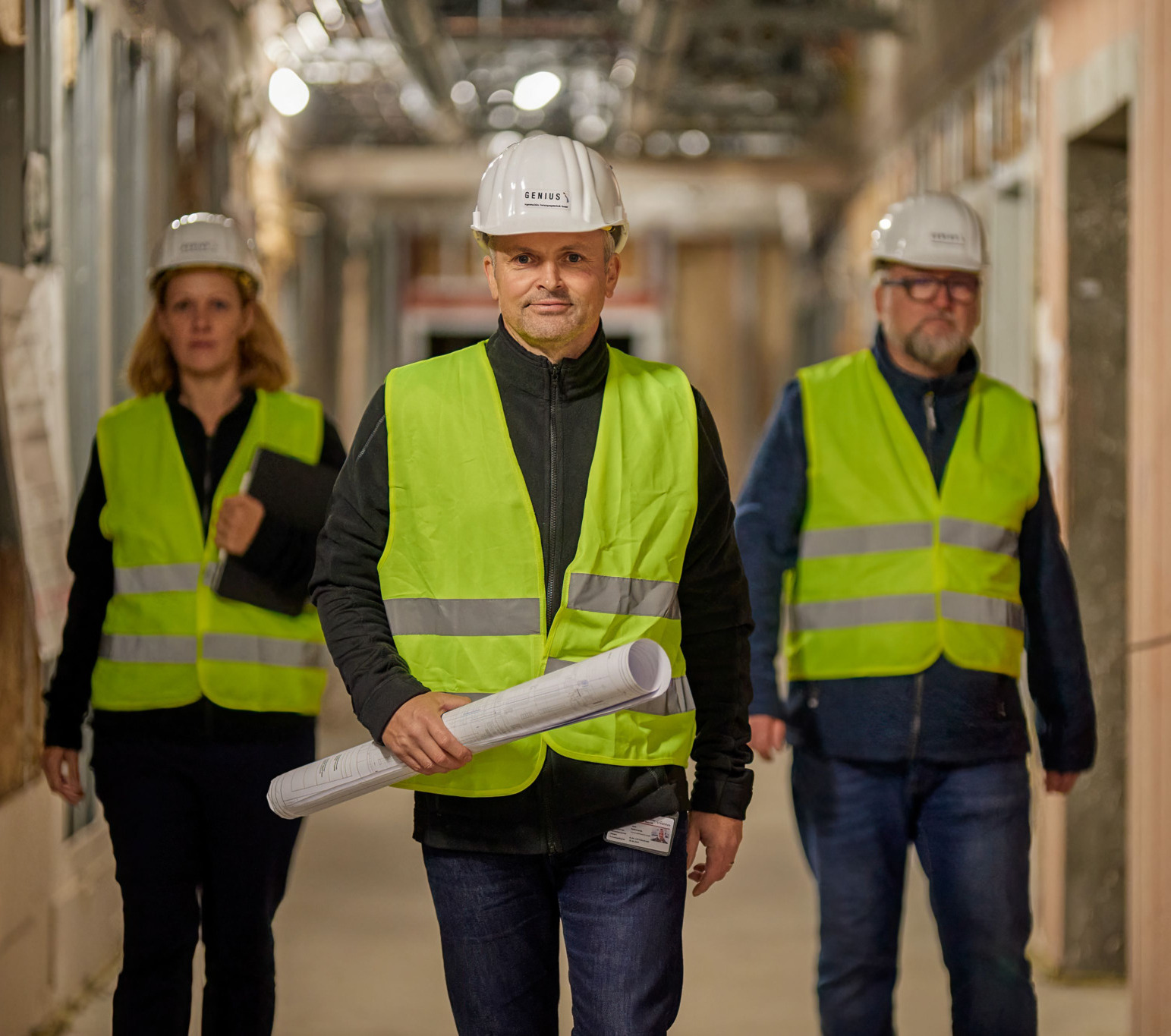 Drei Genius-Mitarbeitende mit Schutzhelmen auf einer Baustelle