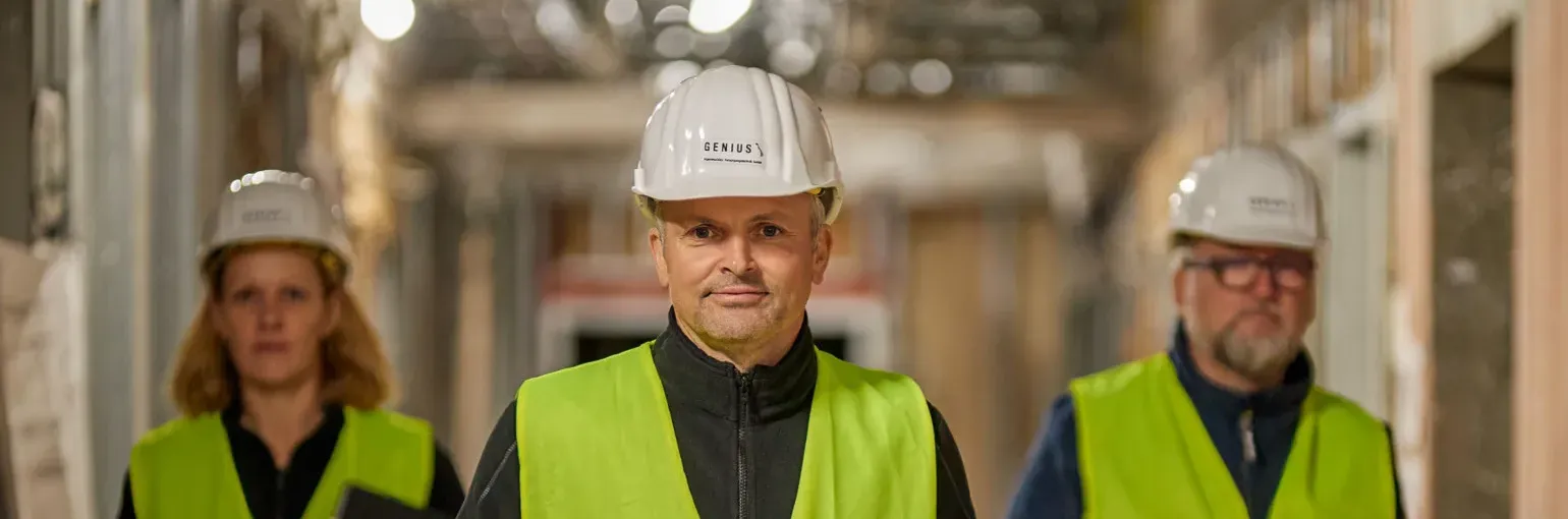 Drei Genius-Mitarbeitende mit Schutzhelmen auf einer Baustelle