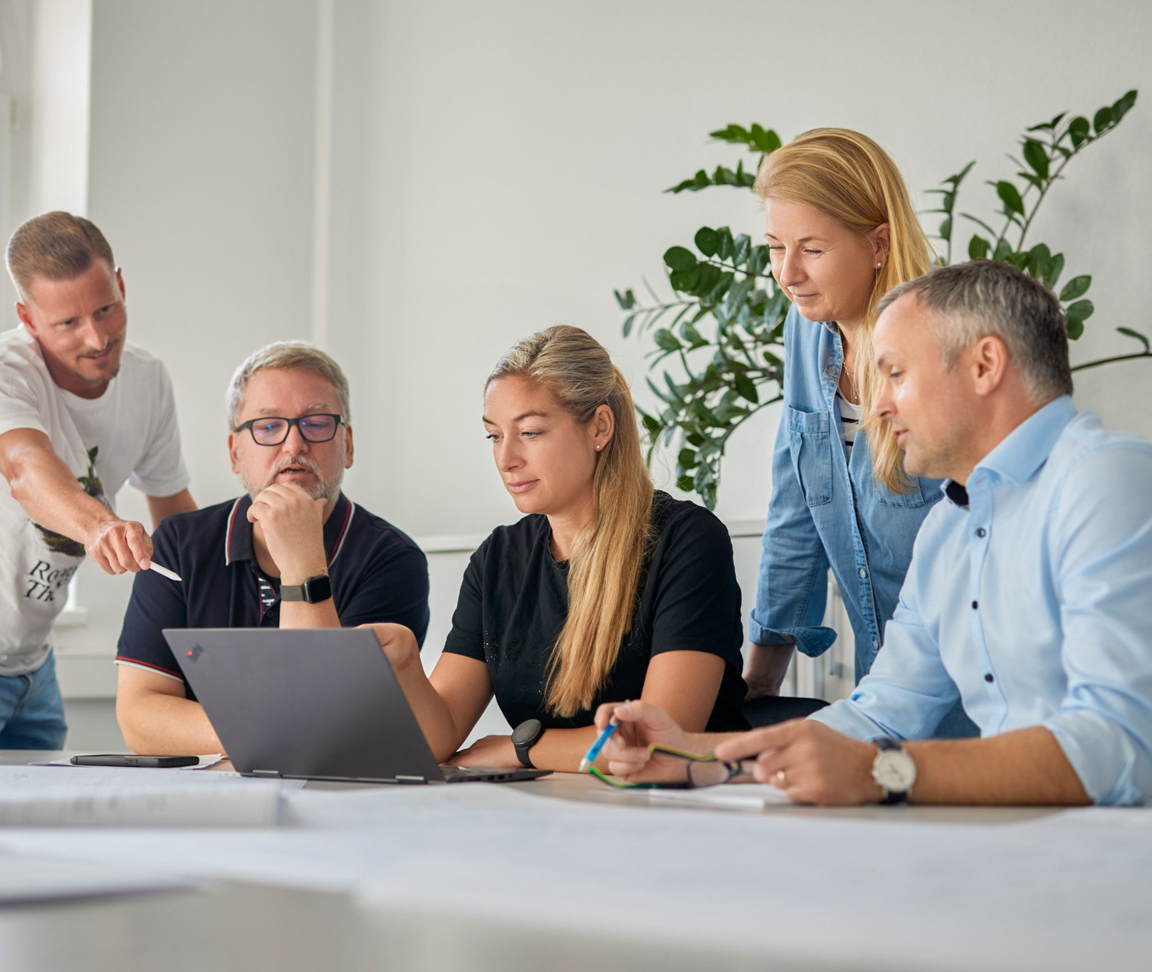 Fünf Genius-Mitarbeitende besprechen ein Projekt am Laptop im Büro